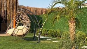 Un bâtiment à toit de chaume, doté d’une chaise suspendue et d’une pelouse bien entretenue.