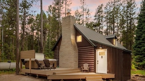 A log cabin with a chimney, a deck with outdoor furniture, and a door with a plaque.