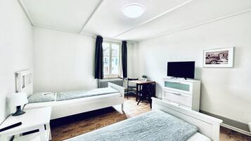 Una habitación pequeña y limpia con dos camas, un escritorio, una silla, un televisor y una ventana con cortinas.