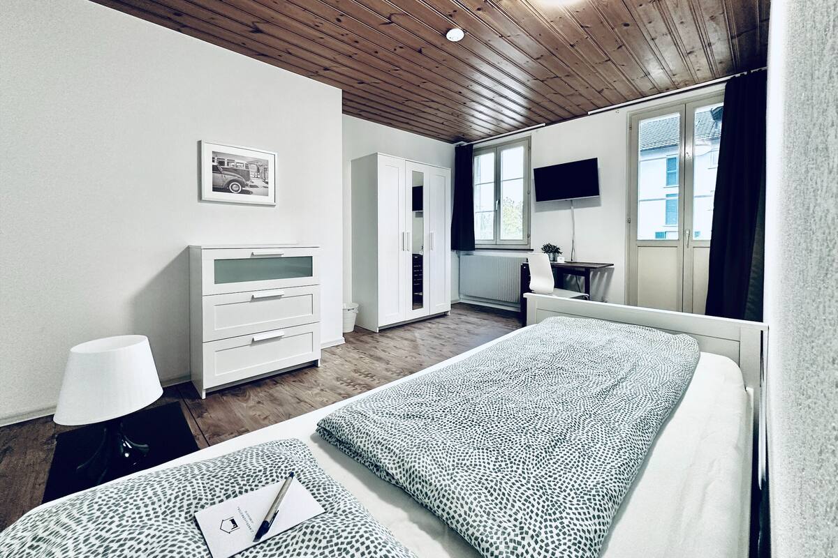 Un dormitorio con cama, cómoda, escritorio, silla, televisor y ventana.
