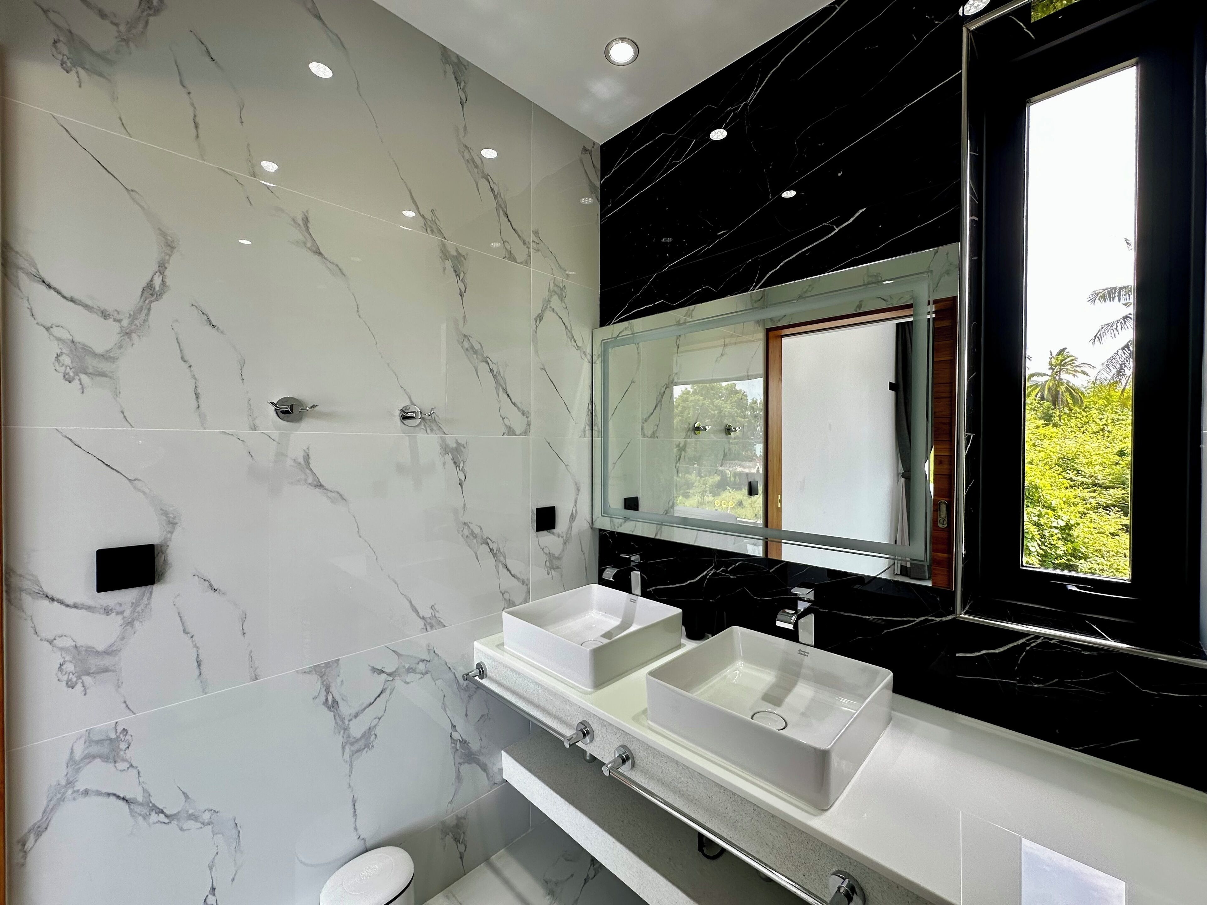 Un baño moderno con dos lavamanos, un espejo grande y una ventana con vistas a zonas verdes.