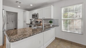 A kitchen with white cabinets, granite countertops, a built-in microwave, and a window with blinds. - Spacious 5-bedroom house in delightful Glendale with WiFi, AC (Glendale)