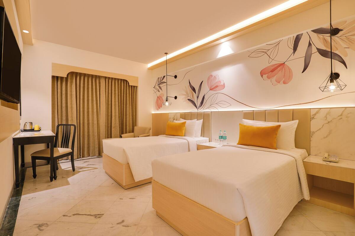 A hotel room with two beds, a desk, a chair, and a large floral mural on the wall.