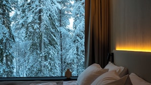 Ein Hotelzimmer mit großem Fenster und Blick auf einen verschneiten Wald.