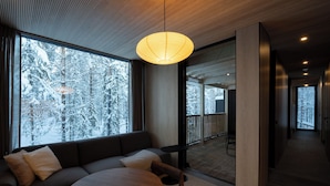 Ein modernes Interieur mit einer Couch, einem runden Tisch und großen Fenstern mit Blick auf einen verschneiten Wald.