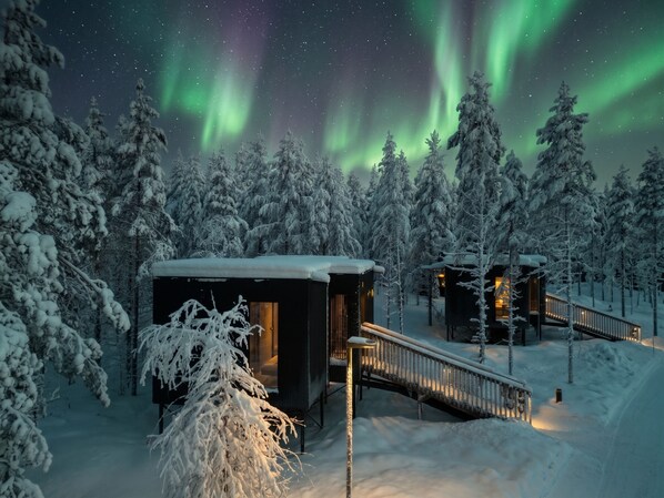 Una cabaña nevada con terraza de madera y puerta de cristal.