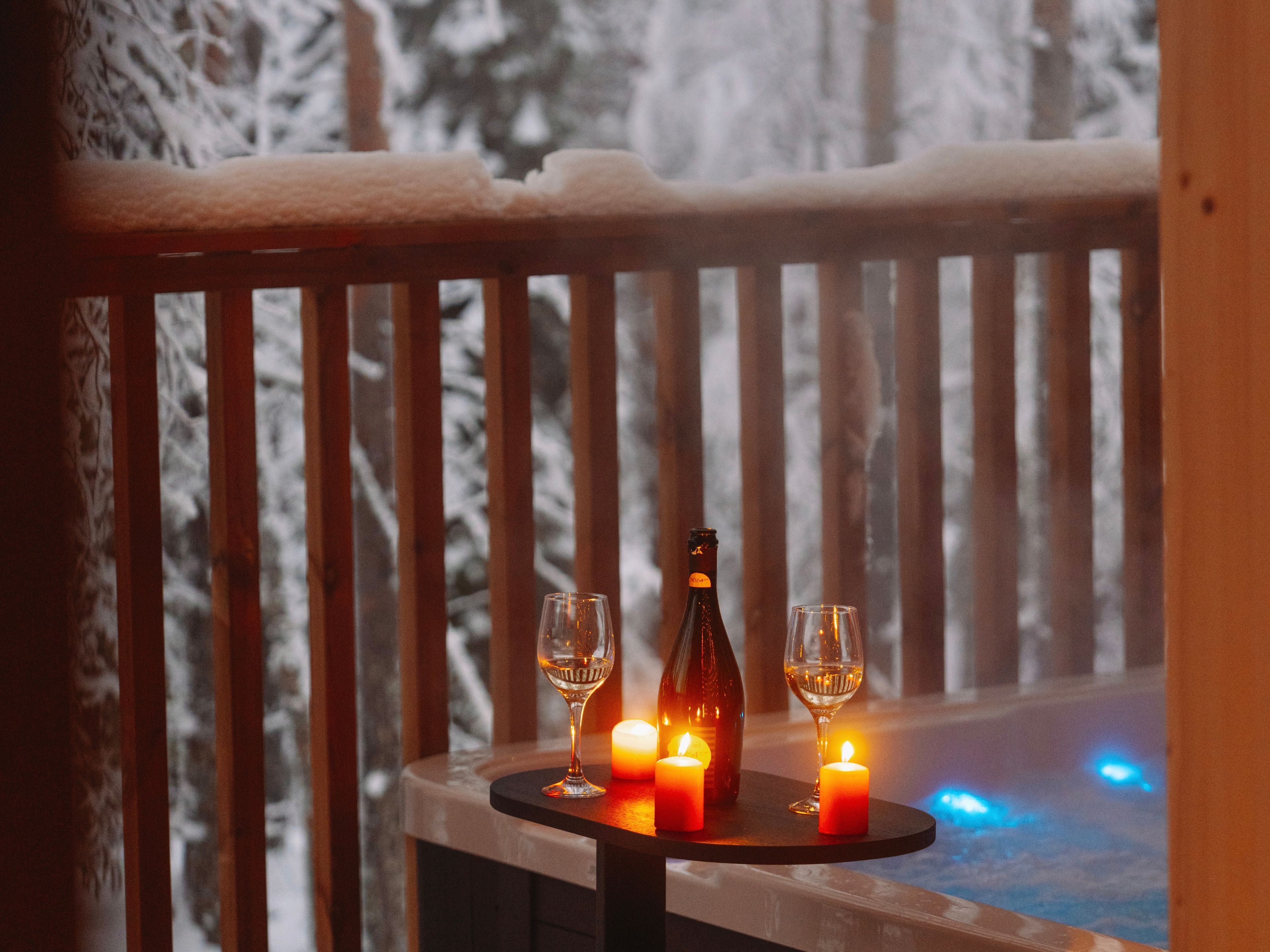 A wooden deck with a table holding a bottle and two glasses, surrounded by candles.