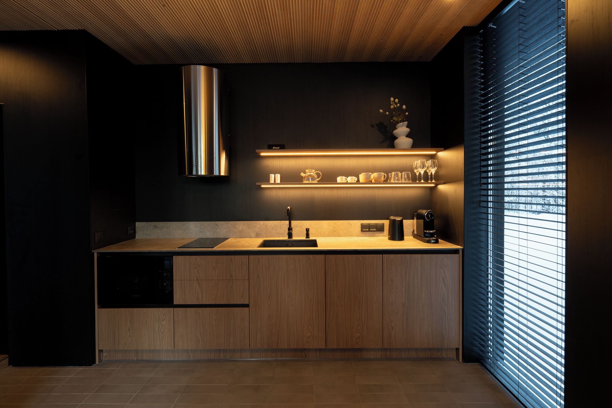 Une cuisine moderne avec des meubles en bois, une hotte en acier inoxydable et une étagère intégrée pour ranger les ustensiles de cuisine.