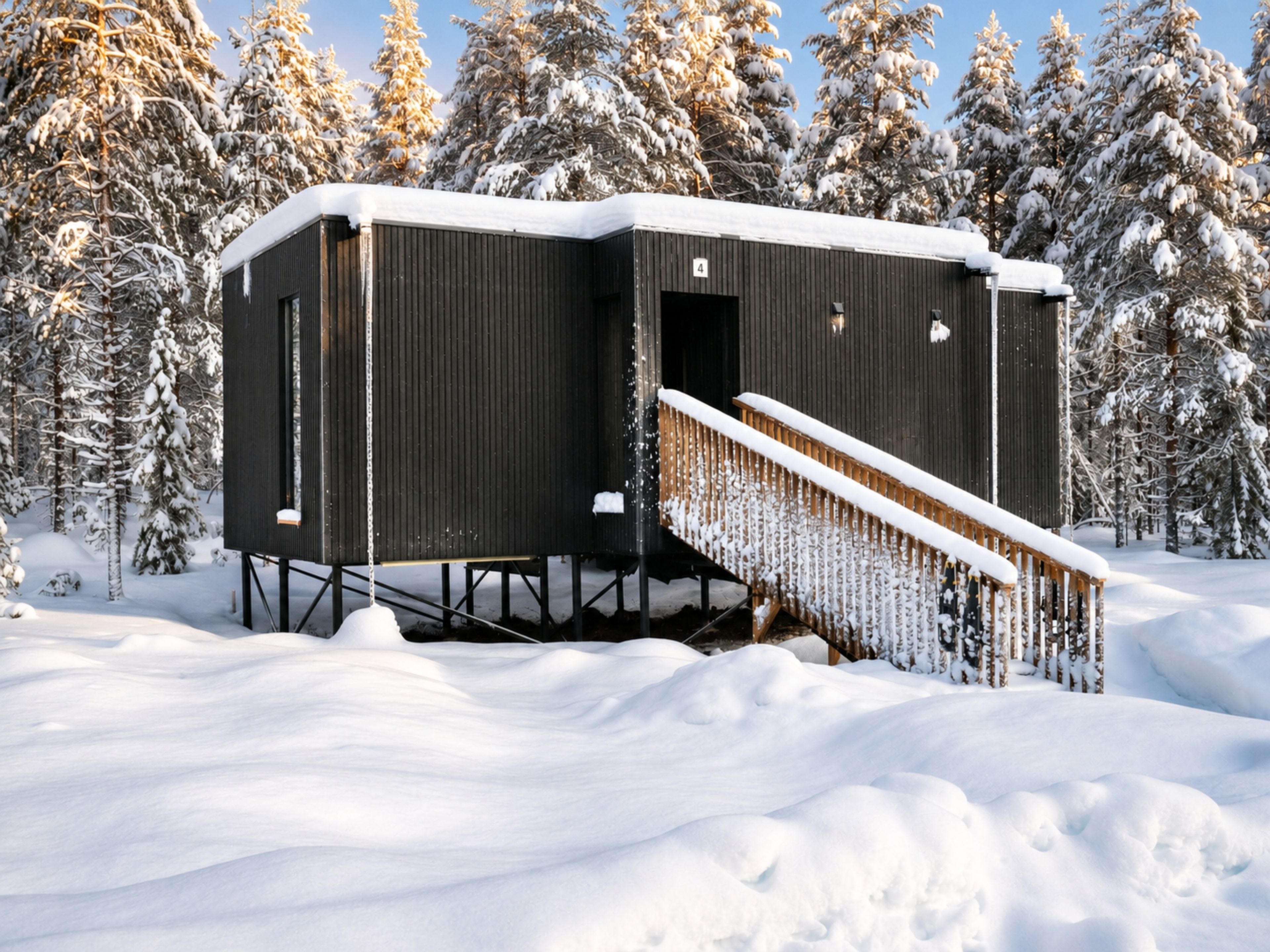 Una cabaña con una escalera de madera que lleva a una puerta, rodeada de árboles cubiertos de nieve.