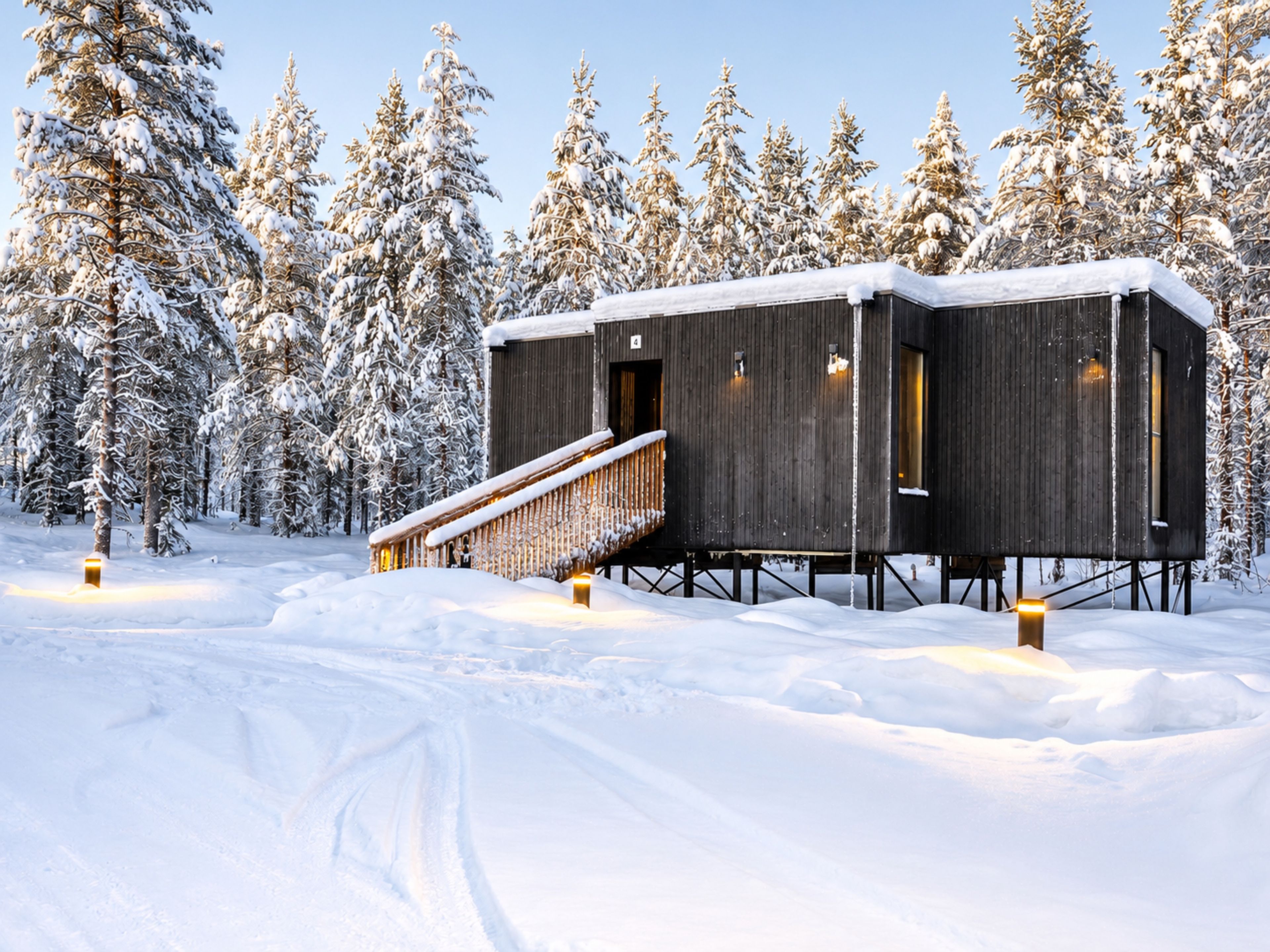 A wooden cabin with a wooden staircase, surrounded by snow-covered trees.