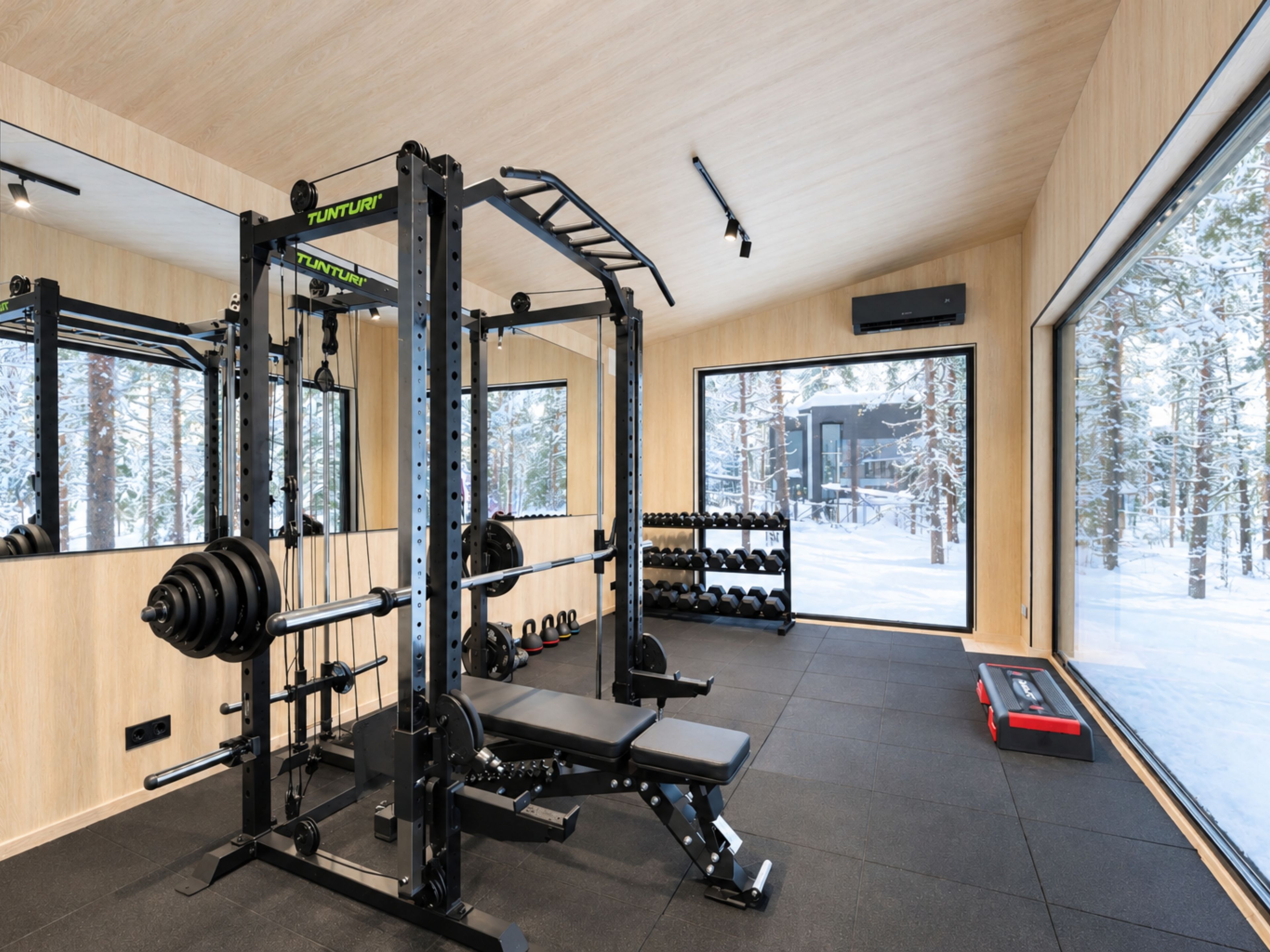 A gym with weightlifting equipment, dumbbells, and a bench.