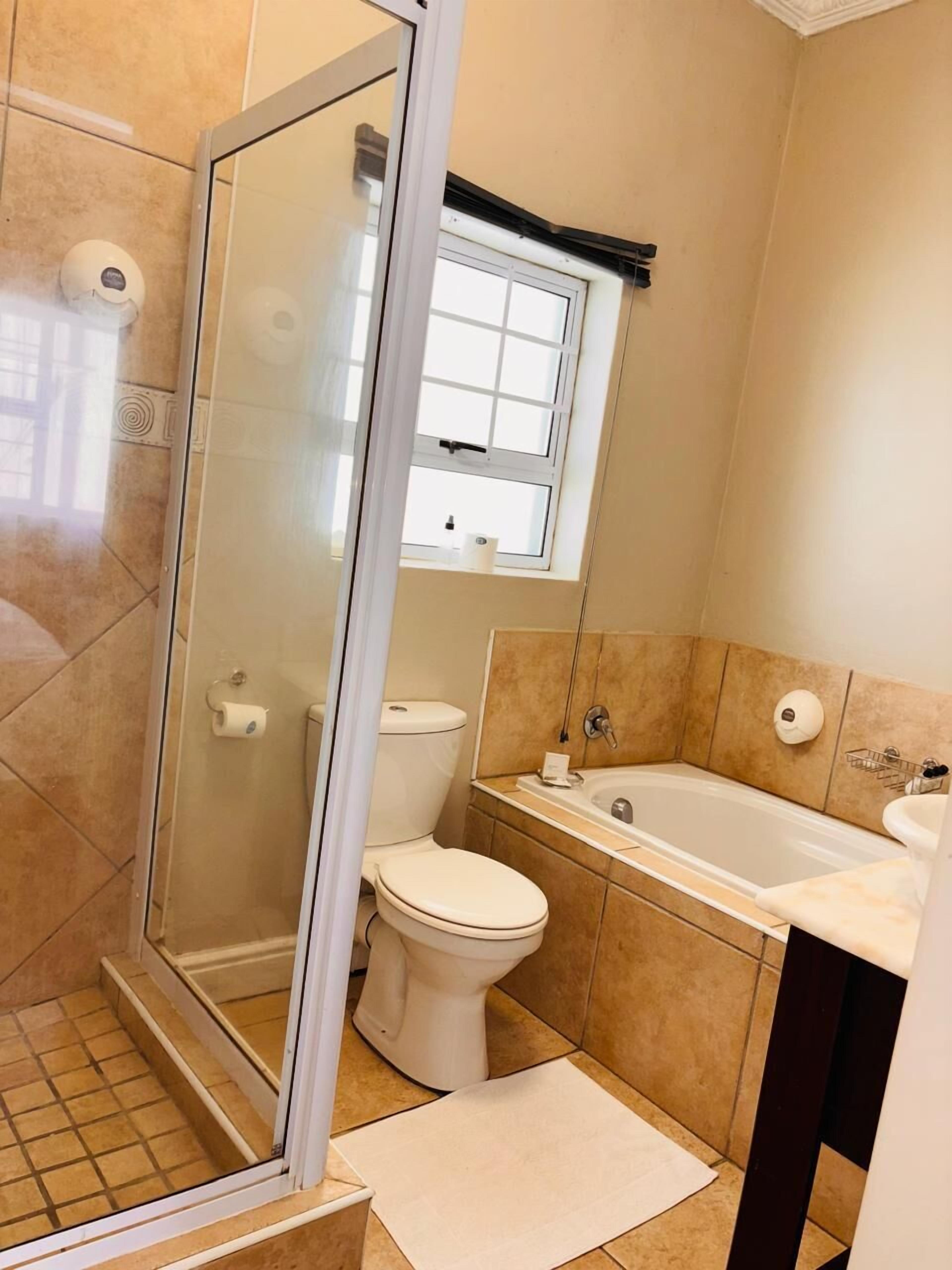 A bathroom with a glass-enclosed shower, a toilet, a bathtub, and a window above the toilet.