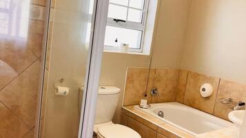 A bathroom with a glass-enclosed shower, a toilet, a bathtub, and a window above the toilet.