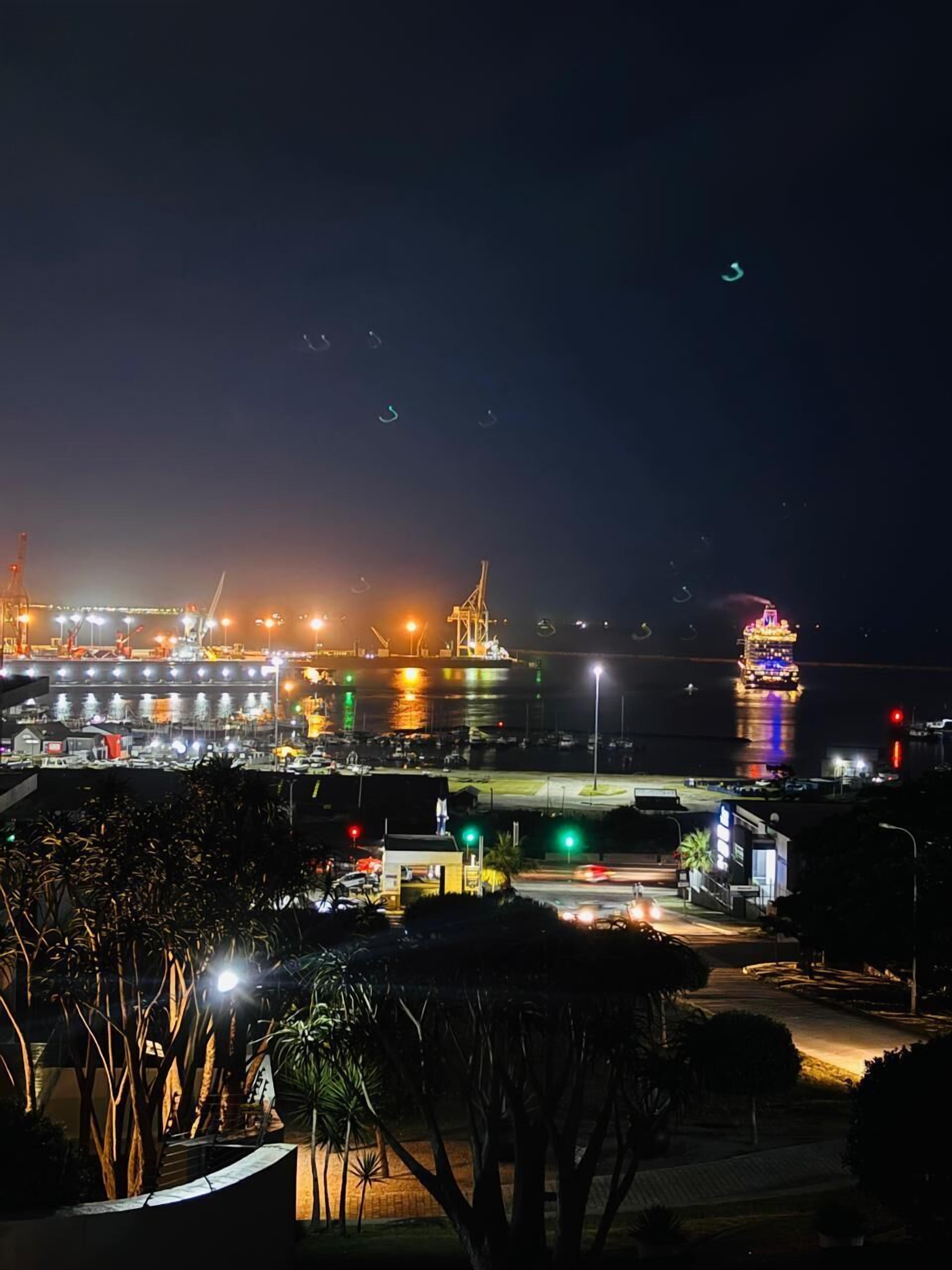 A nighttime view of a waterfront area with illuminated buildings and a bridge.