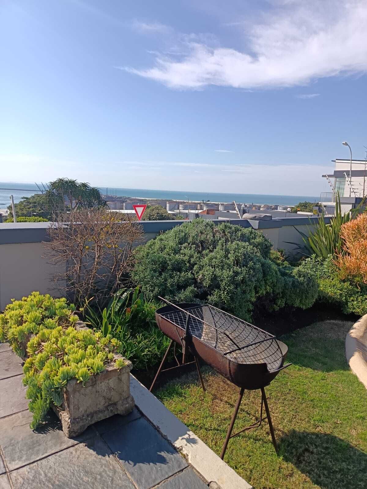Un giardino pensile con una griglia per barbecue, piante in vaso e vista sul mare.
