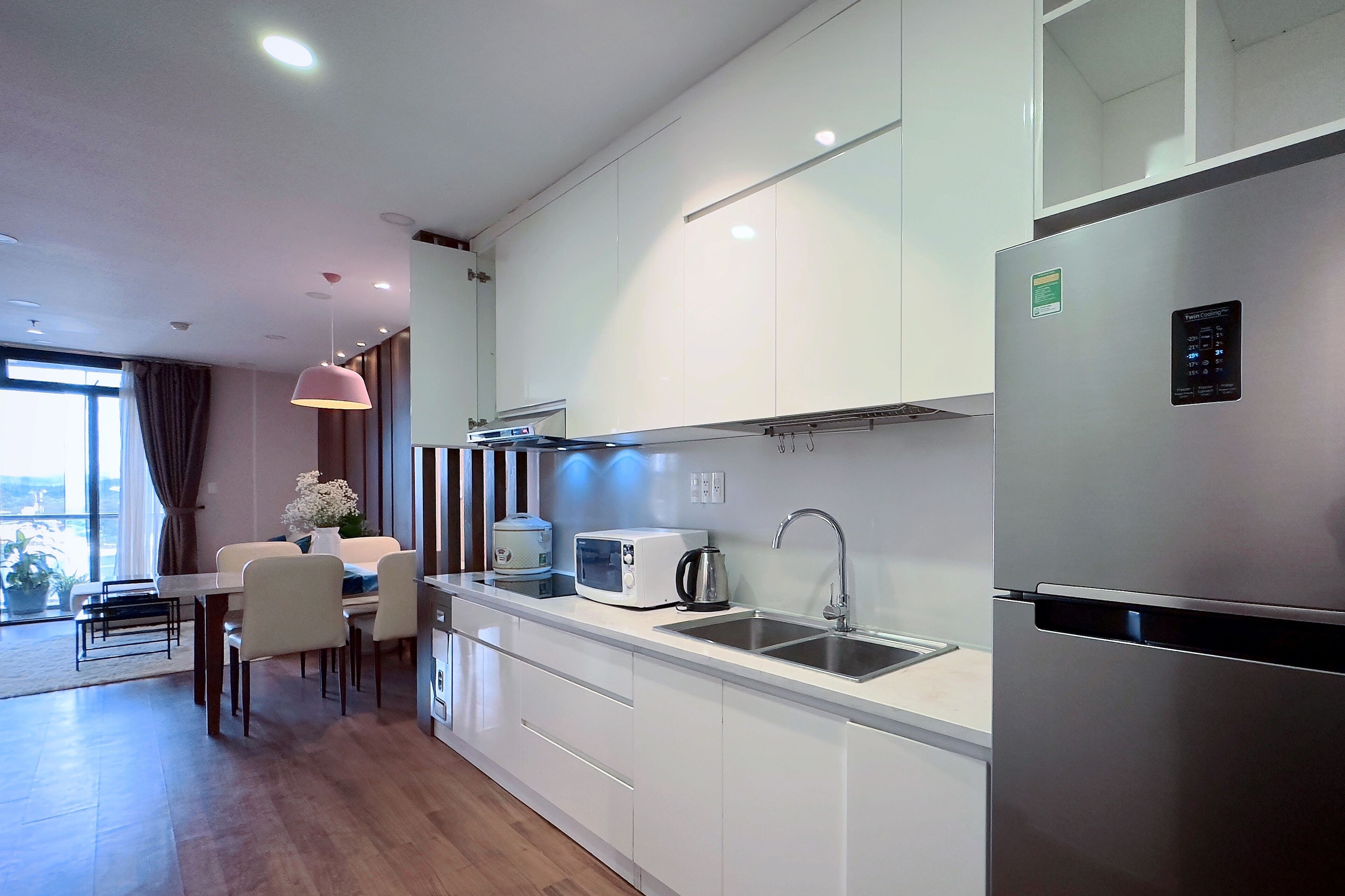 A modern kitchen with white cabinets, stainless steel appliances, a dining area with a table and chairs, and a large window providing natural light.