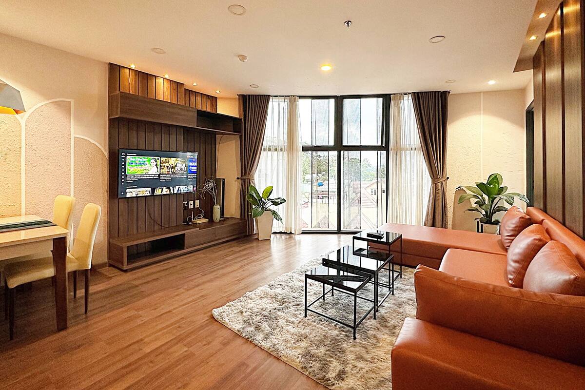 A modern living room with a flat-screen TV, wooden furniture, a sofa, and a dining area.