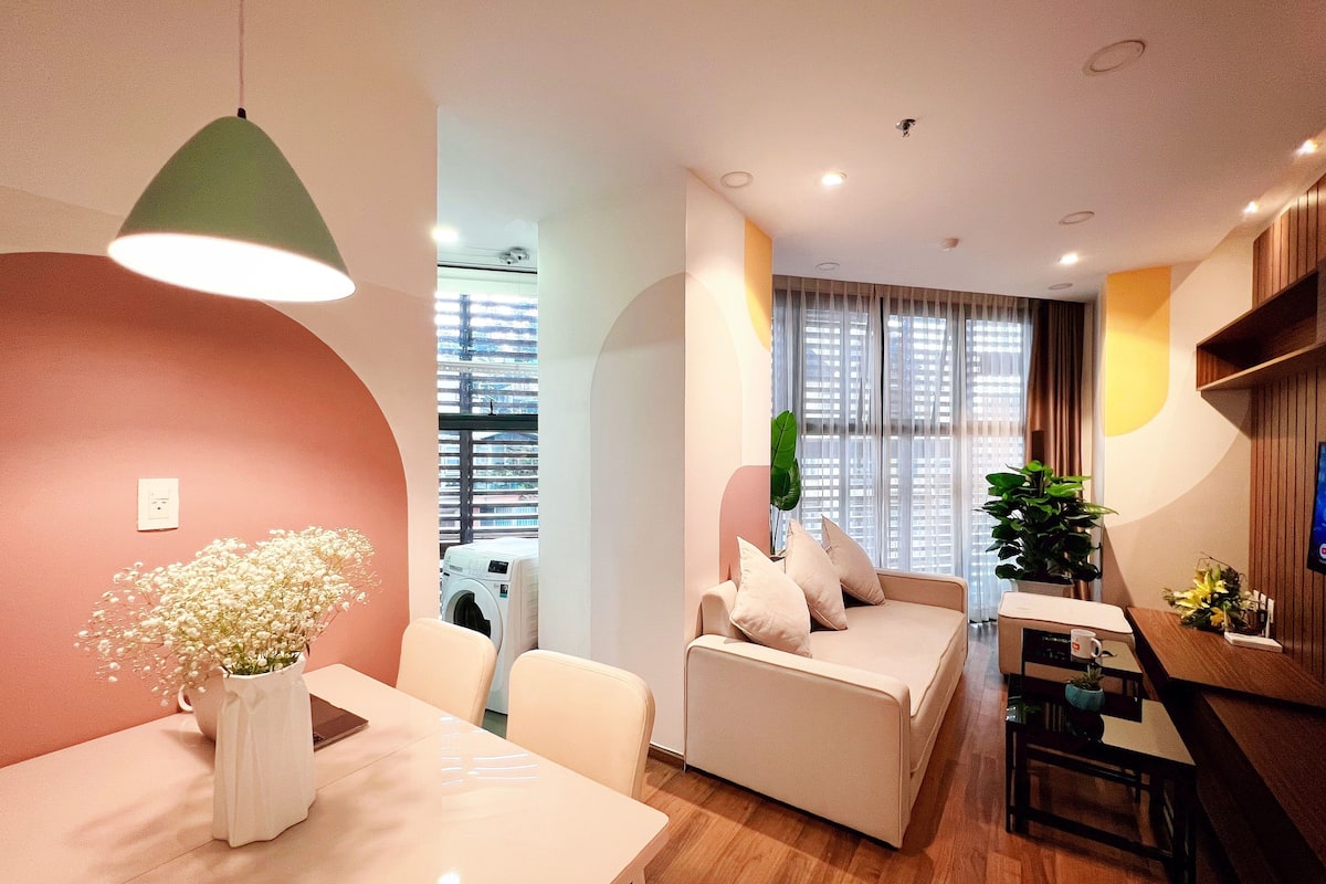 A modern living room with a sofa, a dining table with a vase of flowers, and a hanging lamp.