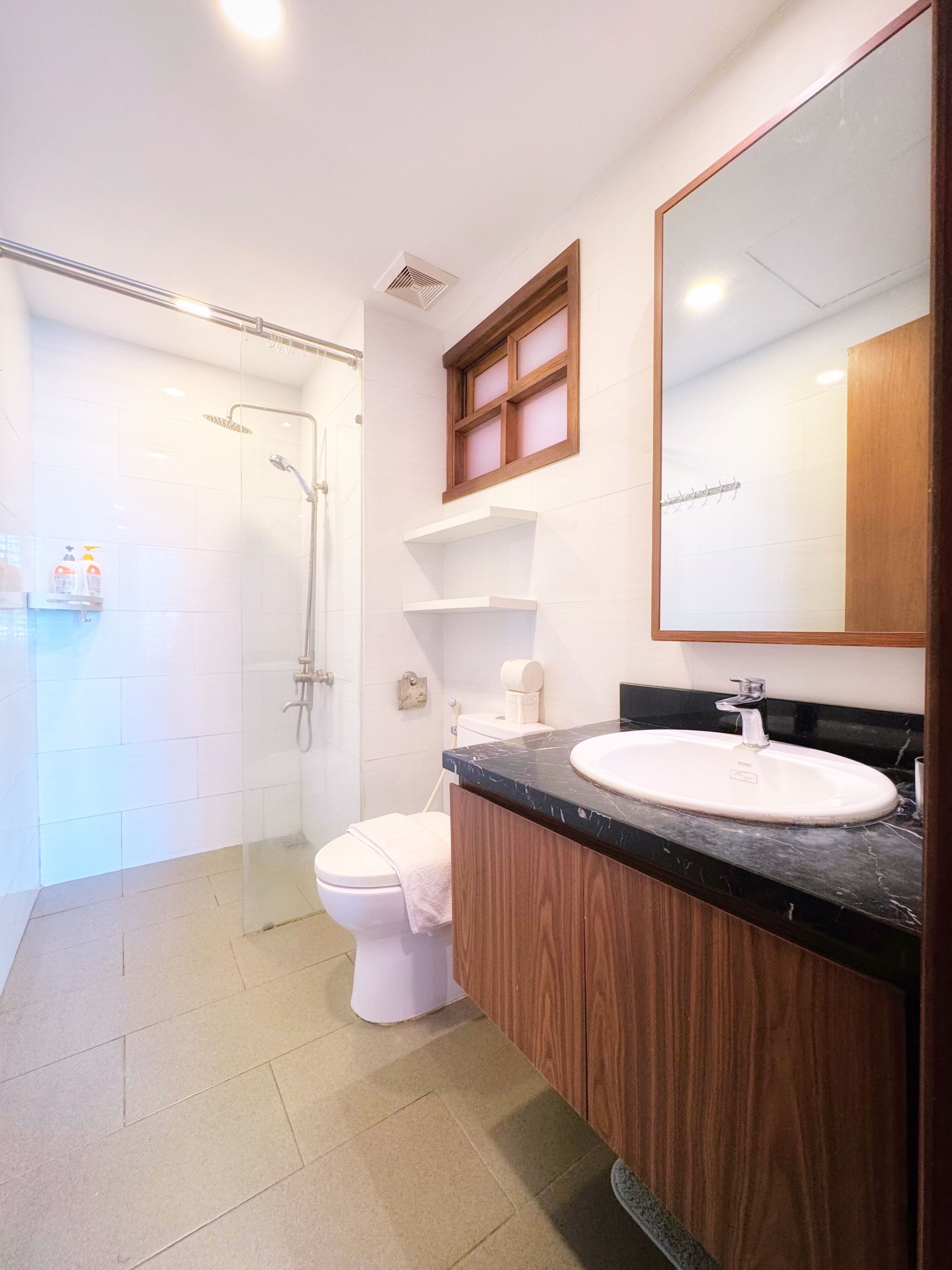 Un baño moderno con ducha de vidrio, inodoro blanco, tocador con encimera negra y un espejo grande.