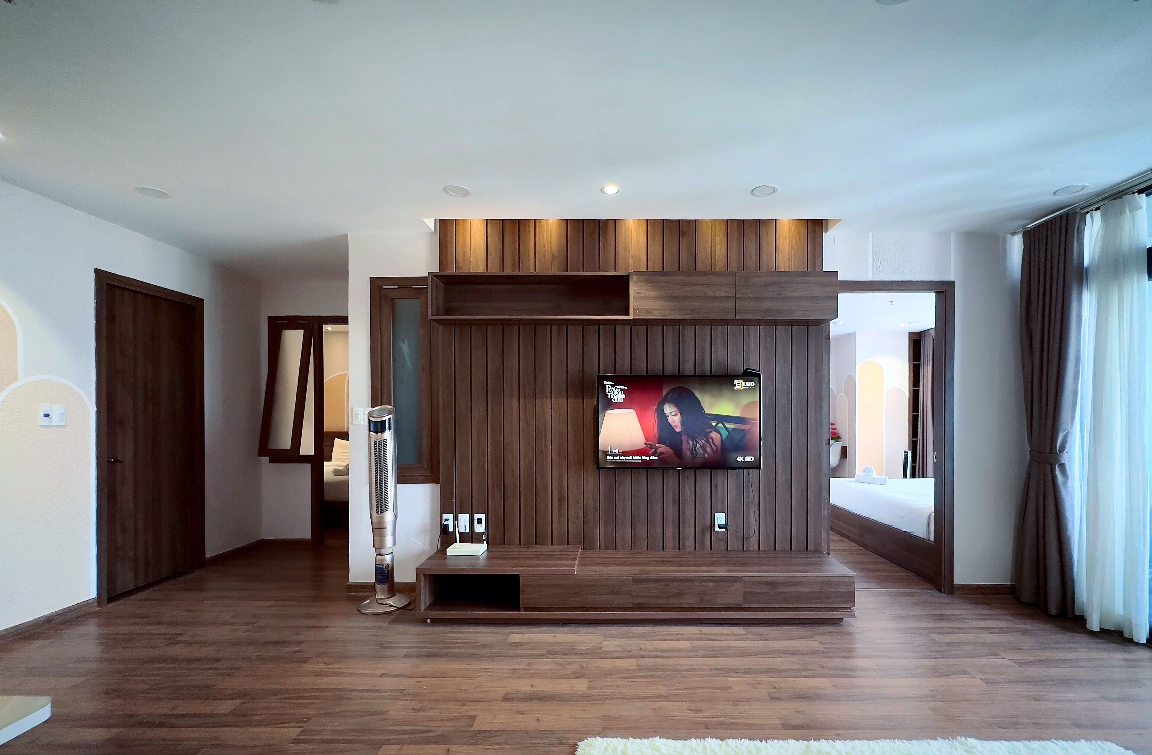 Un salón moderno con televisor empotrado, paneles de madera y un gran ventanal con cortinas.