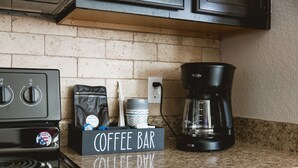 Una encimera de cocina con espacio para café, que incluye una cafetera, una caja con la etiqueta 'Coffee Bar Coffee' y una bolsa de café.