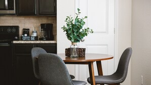 Un comedor con una mesa redonda de madera, dos sillas grises tapizadas y una planta en maceta sobre la mesa.