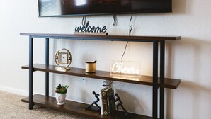 Un televisor de pantalla plana montado en una pared sobre una mesa consola de madera con un letrero de neón que dice "Cheers".