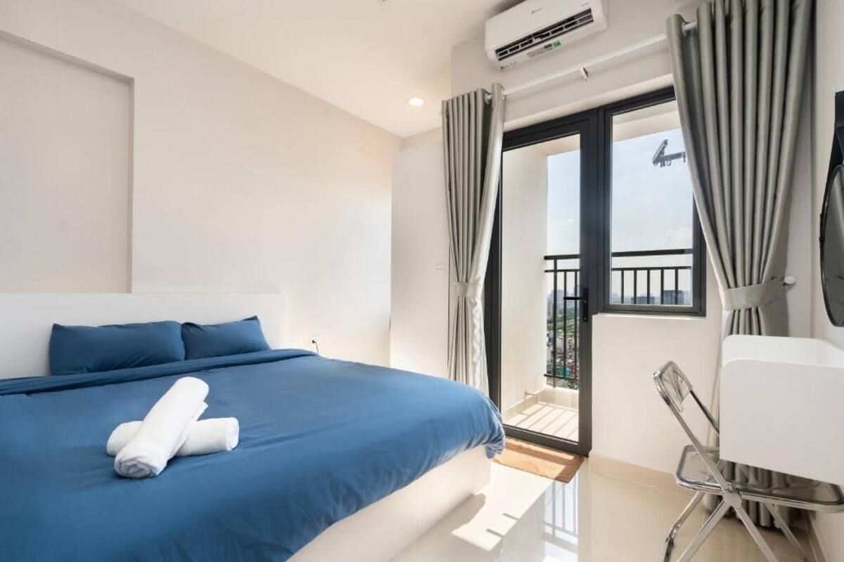 A hotel room with a large bed, a desk, and a balcony with curtains.