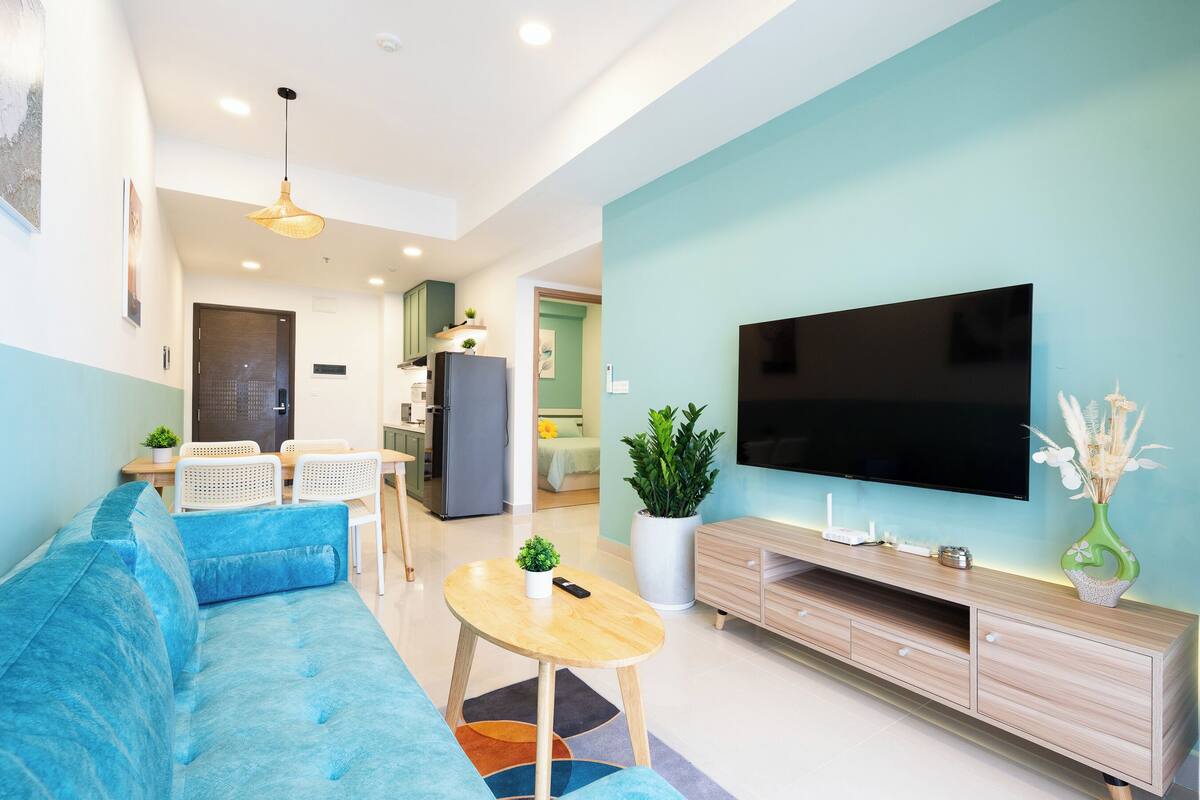 A modern living room with a blue sofa, a wooden coffee table, a flat-screen TV, and a potted plant.