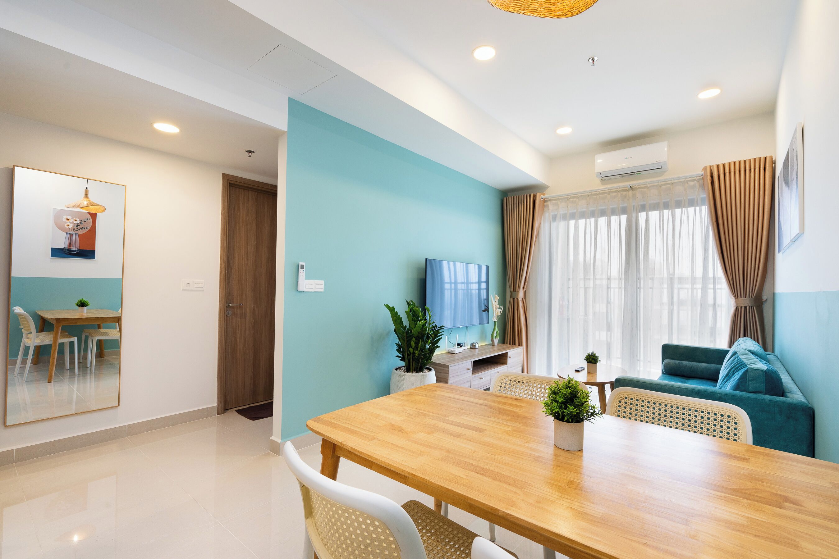 A modern living room with a wooden dining table, teal walls, and a blue sofa.