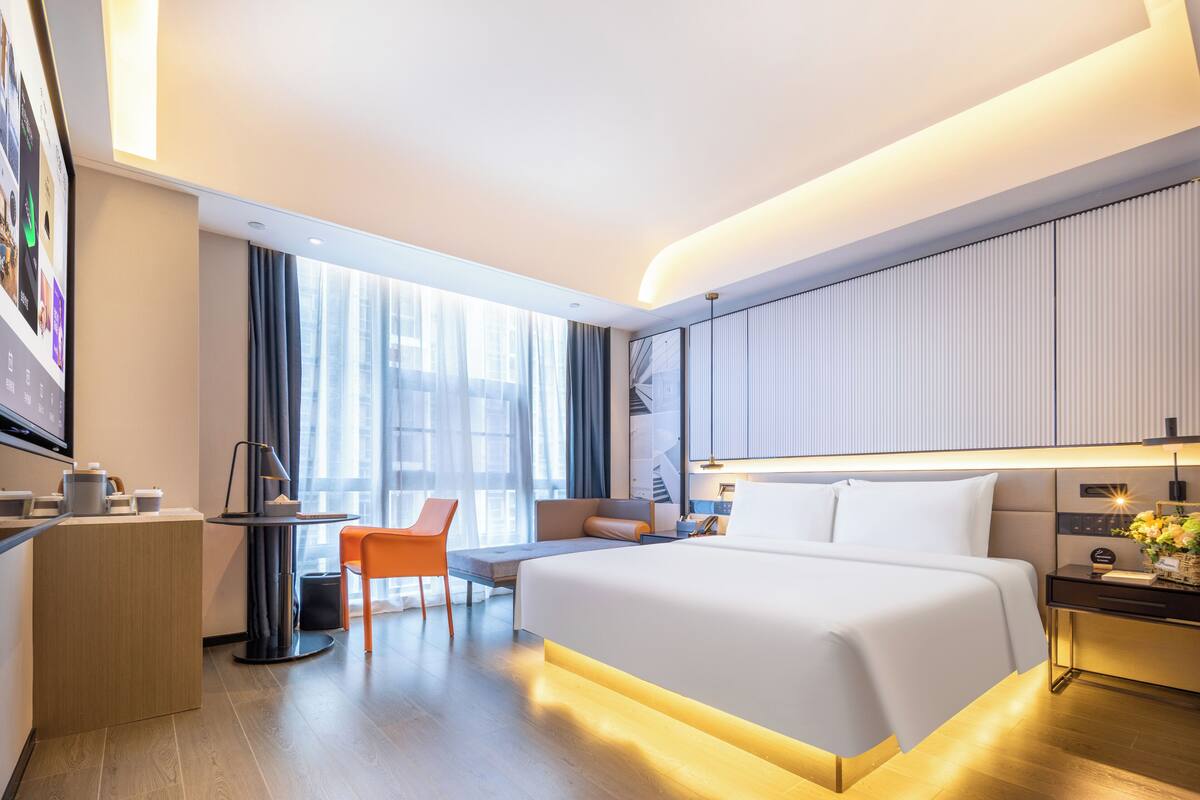 Una habitación de hotel moderna con una cama grande, un escritorio, una silla y un televisor.