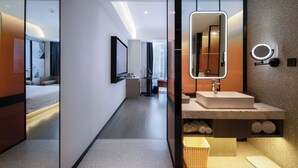 Een moderne hotelbadkamer met een grote spiegel, een wastafel en een klein rieten mandje.