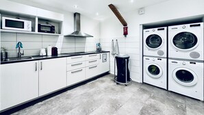 A modern kitchen with white cabinets, a black countertop, a stainless steel range hood, a microwave, a toaster, and a washing machine. - ZIMMERzuVERMIETEN.ch Oensingen (Oensingen)