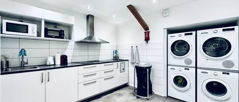 Une cuisine moderne avec des armoires blanches, un plan de travail noir, une hotte en acier inoxydable, un four à micro-ondes, un grille-pain et un lave-linge.