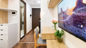 A modern hotel room with a wooden floor, a large flat-screen TV displaying a scenic landscape, a wooden desk with a vase of flowers, and a chair. - SaiGon Rivergate (Ho Chi Minh City)