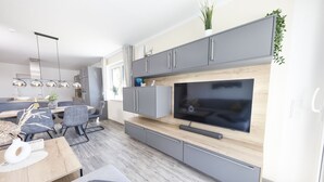 A modern kitchen with grey cabinets, a large TV, and a dining area with a table and chairs. - Apartment 6 "Petra" (Sankt Andreasberg)