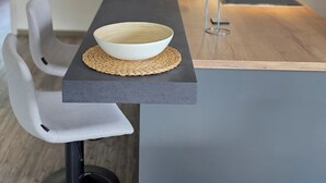 A modern kitchen with a central island, two white chairs, a black chair, and a woven placemat. - Apartment 6 "Petra" (Sankt Andreasberg)
