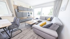 A modern living room with a sofa, chairs, a coffee table, and a kitchen area with cabinets and a countertop. - Apartment 6 "Petra" (Sankt Andreasberg)