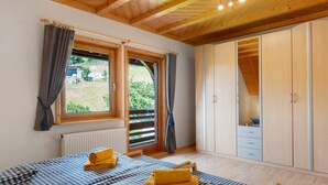 Une chambre à coucher avec un lit, deux fenêtres, une armoire et une vue sur la verdure.