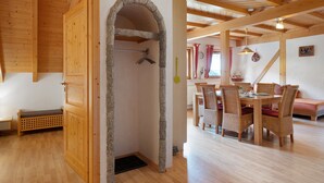 Une pièce aux murs en bois, dotée d’une arche en pierre, d’un coin repas avec des chaises en osier et d’un banc.