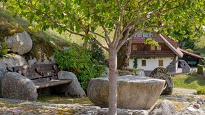 Un banc en pierre, un arbre et un bâtiment rustique doté d’un toit en pente.