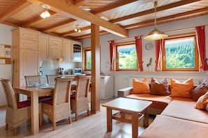 A cozy kitchen with wooden cabinets, a dining table with chairs, and a sofa with orange cushions. - Apartment '2' with Mountain View, Shared Terrace and Wi-Fi (Triberg im Schwarzwald)