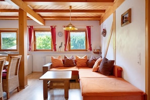 A cozy room with a wooden ceiling, a sofa with cushions, a dining table, and a window with curtains. - Apartment '2' with Mountain View, Shared Terrace and Wi-Fi (Triberg im Schwarzwald)