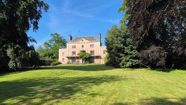 A large, rectangular building with a symmetrical facade, surrounded by lush greenery and trees.