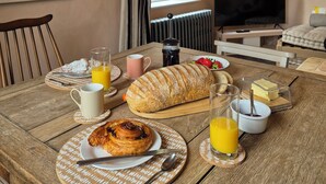 A dining table set with breakfast items including bread, pastries, and juice, in a room with a large painting, a TV, and a window.