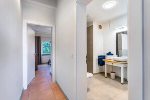 Pasillo que conduce a un baño con inodoro, lavabo y espejo.
