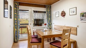 A dining area with a wooden table and chairs, a window with curtains, and wall-mounted pictures.
