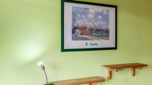 A framed painting of a winter landscape on a green wall, a desk lamp, and two wooden benches.