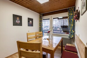 A dining area with a wooden table and chairs, a vase with flowers, and a window with curtains.