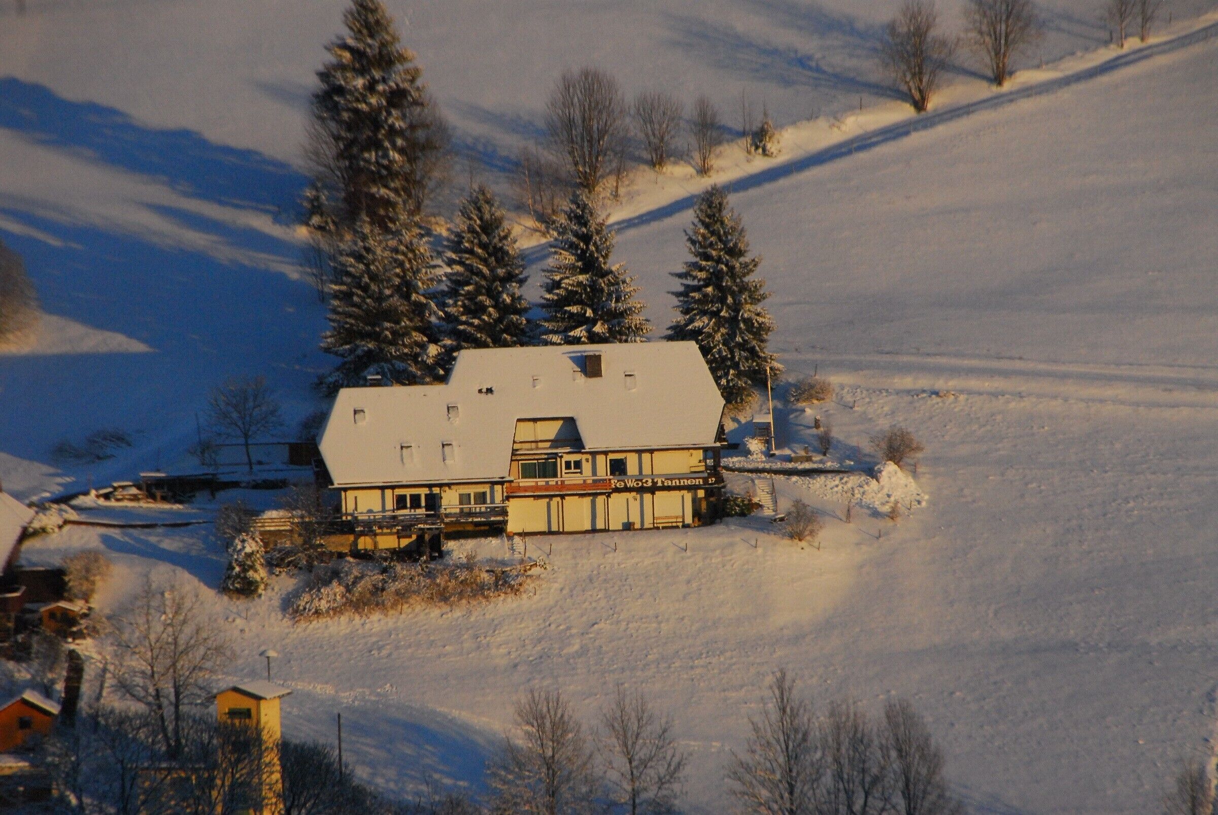 Un edificio cubierto de nieve con techo inclinado, rodeado de árboles y un paisaje nevado.